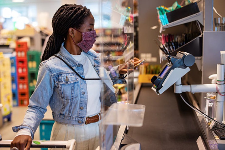 Une femme place son téléphone portable sur un lecteur de carte de crédit à la caisse d'une épicerie. Luis Alvarez via Gettyimages