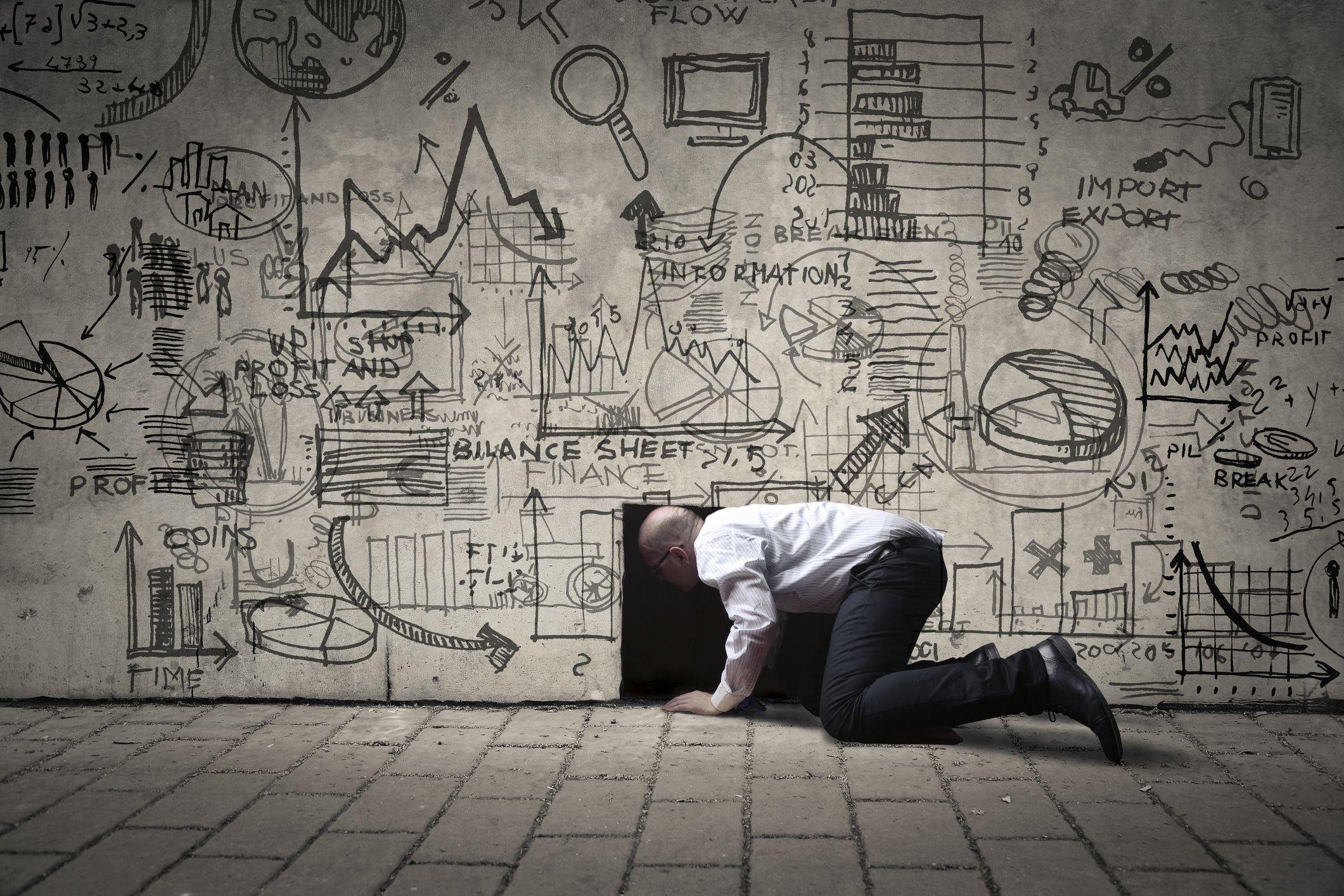 Homme d'affaires rampant dans un petit trou noir, avec des illustrations sur le mur. Photo : bowie15/iStock